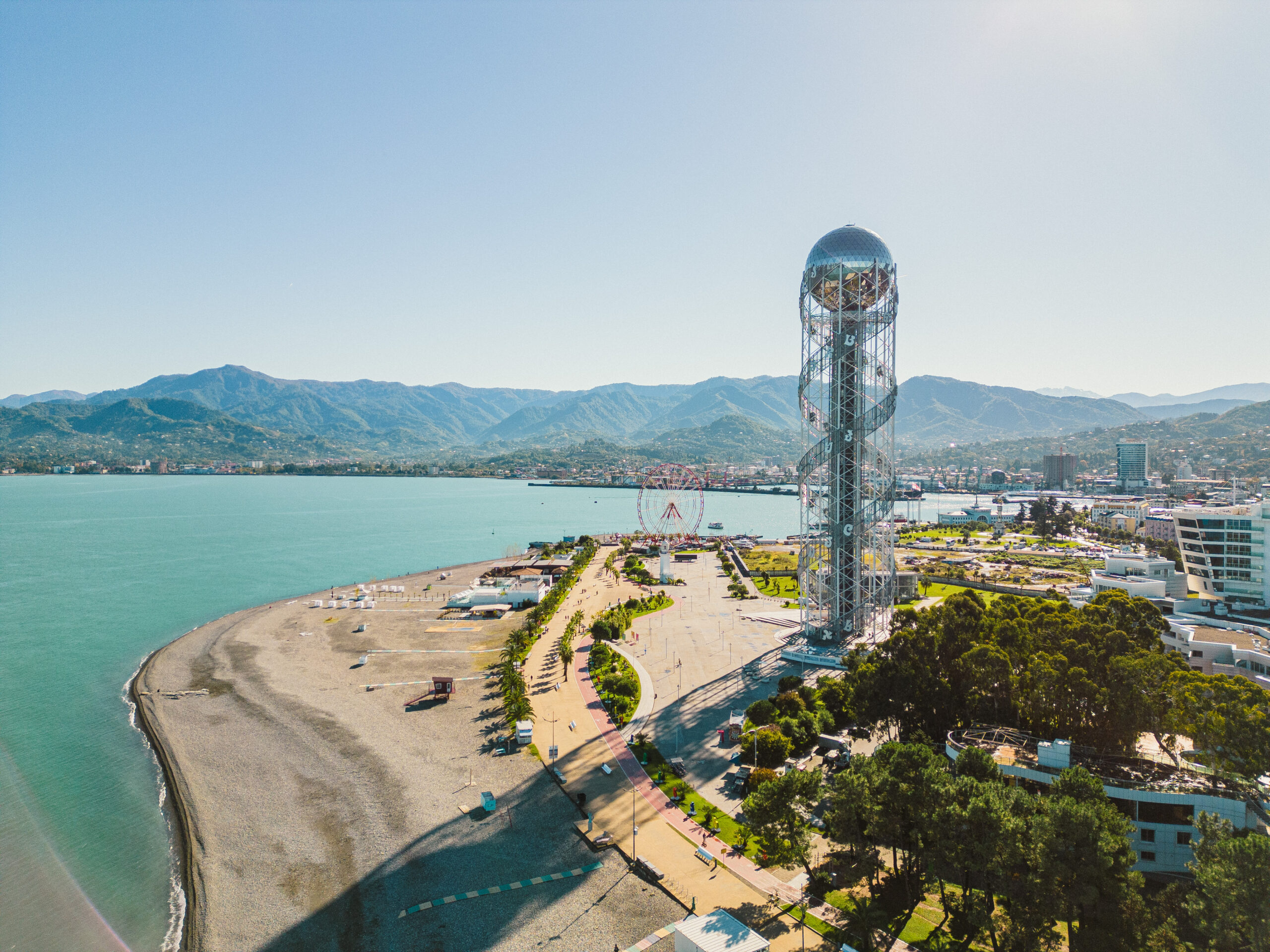 Batumi. Widok na wieżę alfabetu - wysoką konstrukcją ze szklaną kulą na górze, plażę i fragment Morza Czarnego. W tle góry.